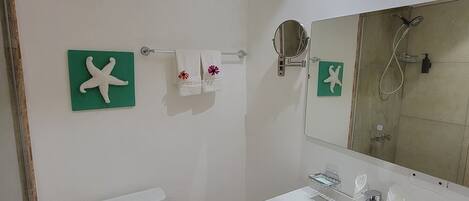 A bathroom with a toilet, sink, mirror, and shower. There are starfish decorations on the wall.
