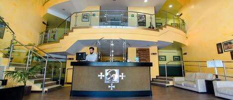 A hotel lobby with a reception desk, multiple staircases, and seating areas.