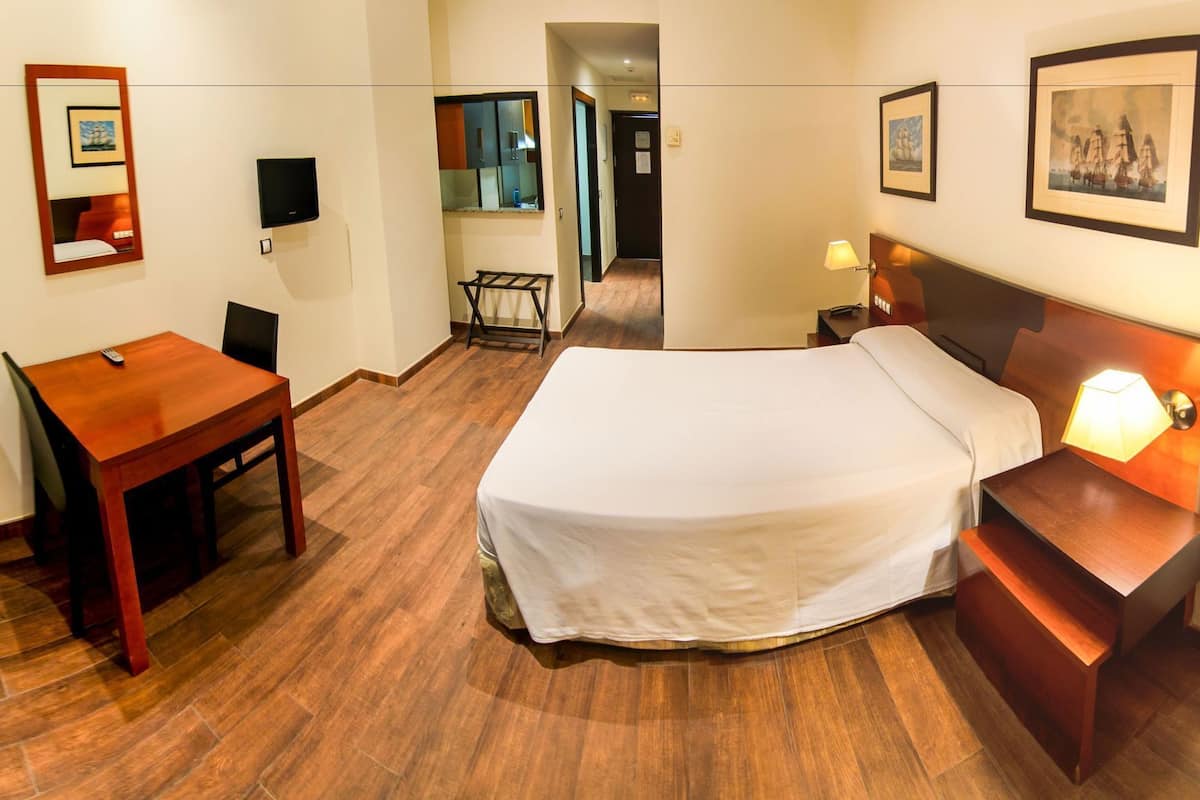 A hotel room with a bed, a desk, a chair, a TV, and a lamp.