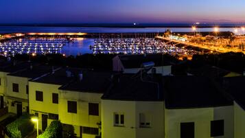 A marina at dusk with boats docked, buildings with balconies, and a clear view of the water.