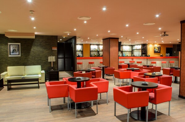 A modern bar area with red and black bar stools, a counter with a variety of bottles, and a seating area with red chairs and a sofa. - Apartamentos Martin Alonso Pinzón (Palos de la Frontera)