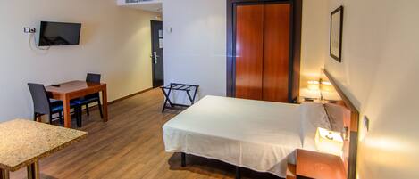 Una habitación de hotel con una cama, un escritorio con silla, un televisor montado en la pared y una puerta.