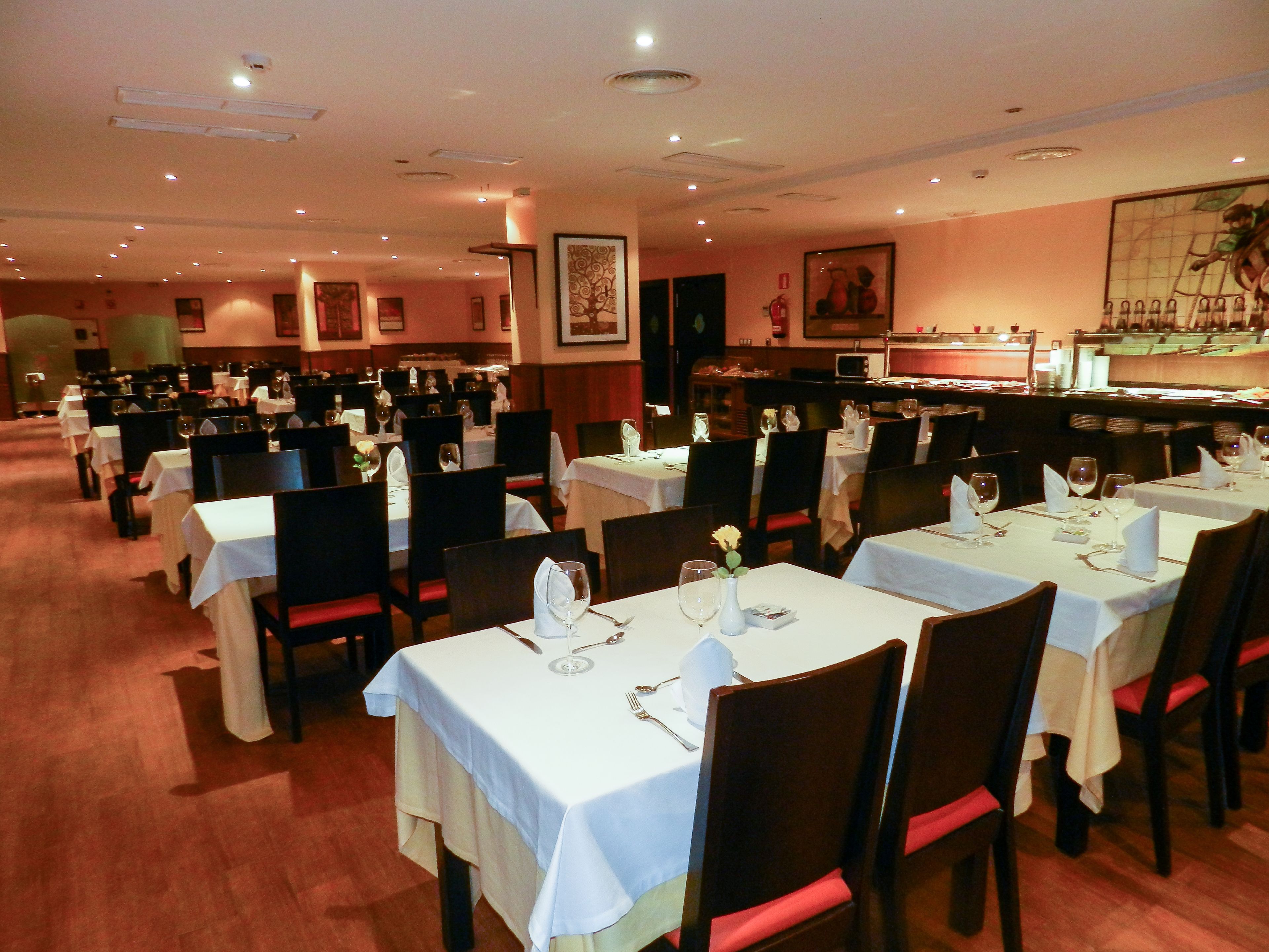A restaurant with multiple tables set for dining, each with white tablecloths and red chair cushions.