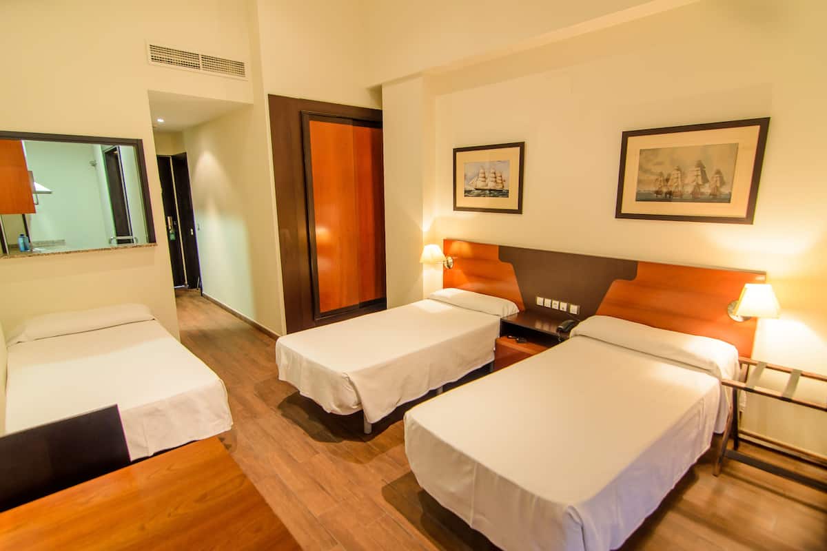A hotel room with two single beds, wooden flooring, a wooden headboard, a nightstand with a lamp, and a framed picture on the wall.