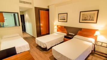 A hotel room with two single beds, wooden flooring, a wooden headboard, a nightstand with a lamp, and a framed picture on the wall.