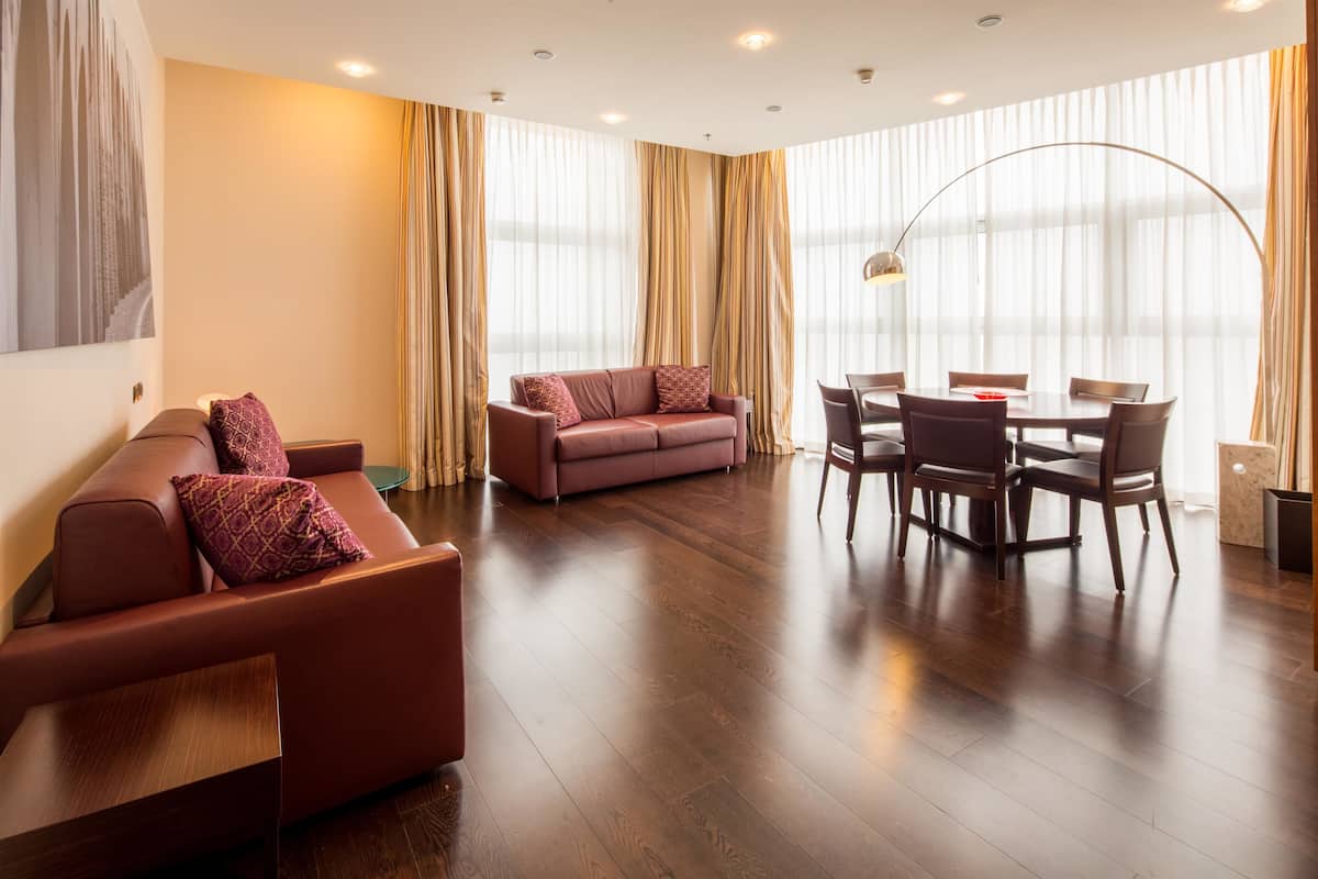 Una sala de estar moderna con un sofá, una mesa de comedor con sillas y ventanas amplias con cortinas.