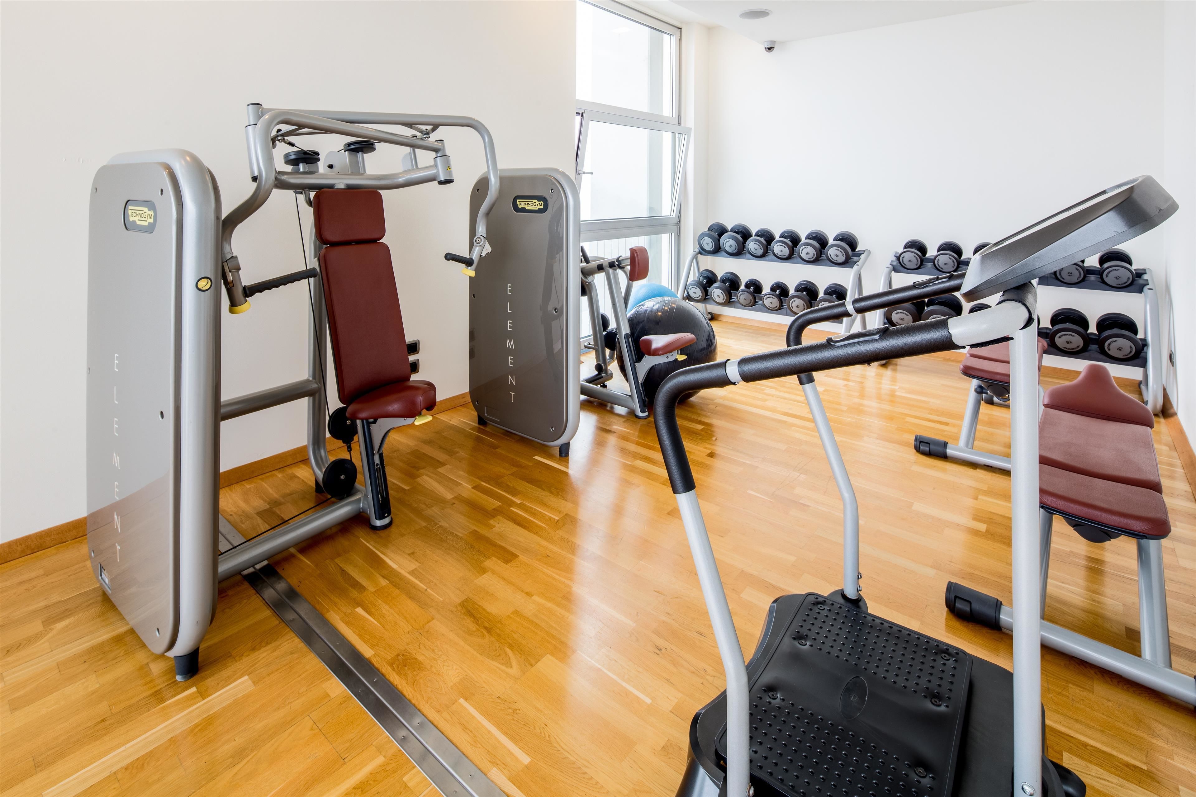 A gym with exercise equipment, a rack of dumbbells, and a wooden floor.