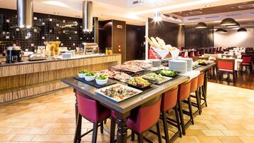 Montaje tipo bufé con diferentes opciones de comida, una zona de bar y disposición de mesas.