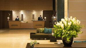 Zona de recepción con mostrador, dos empleados, un sofá y un arreglo floral grande.