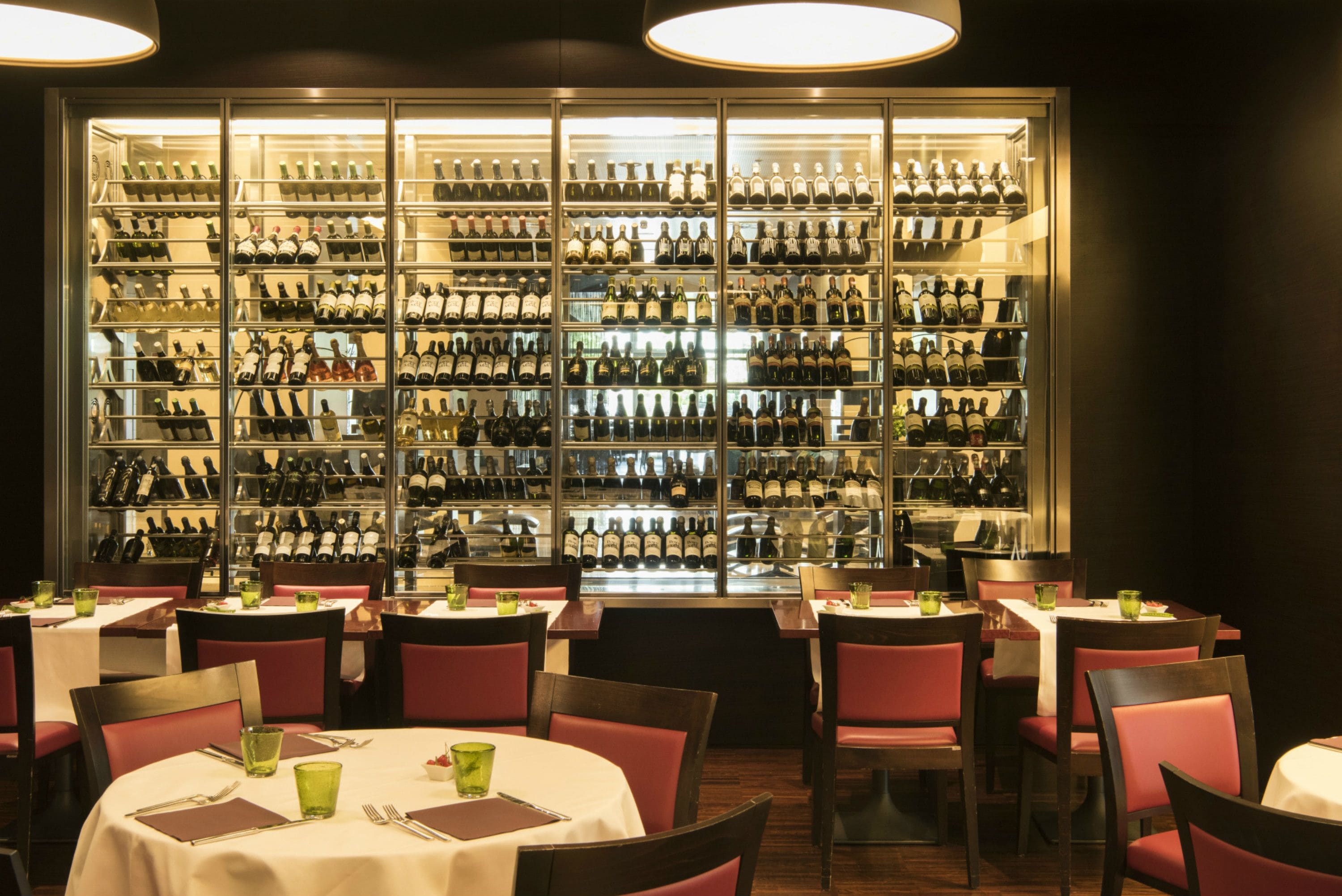A restaurant with tables and chairs, a large wine display case, and a well-lit interior.