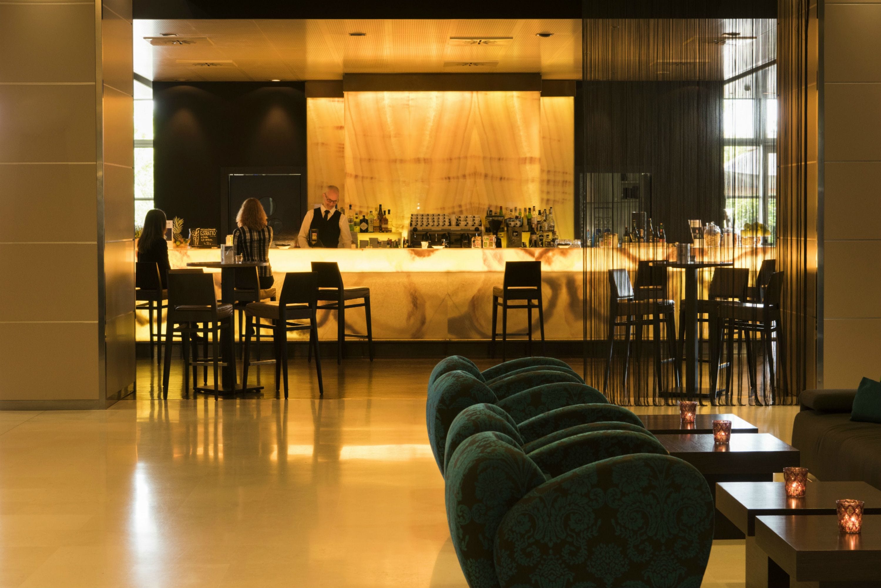 Un espace bar comprenant un comptoir, des tabourets de bar et un coin salon avec des canapés et des tables.