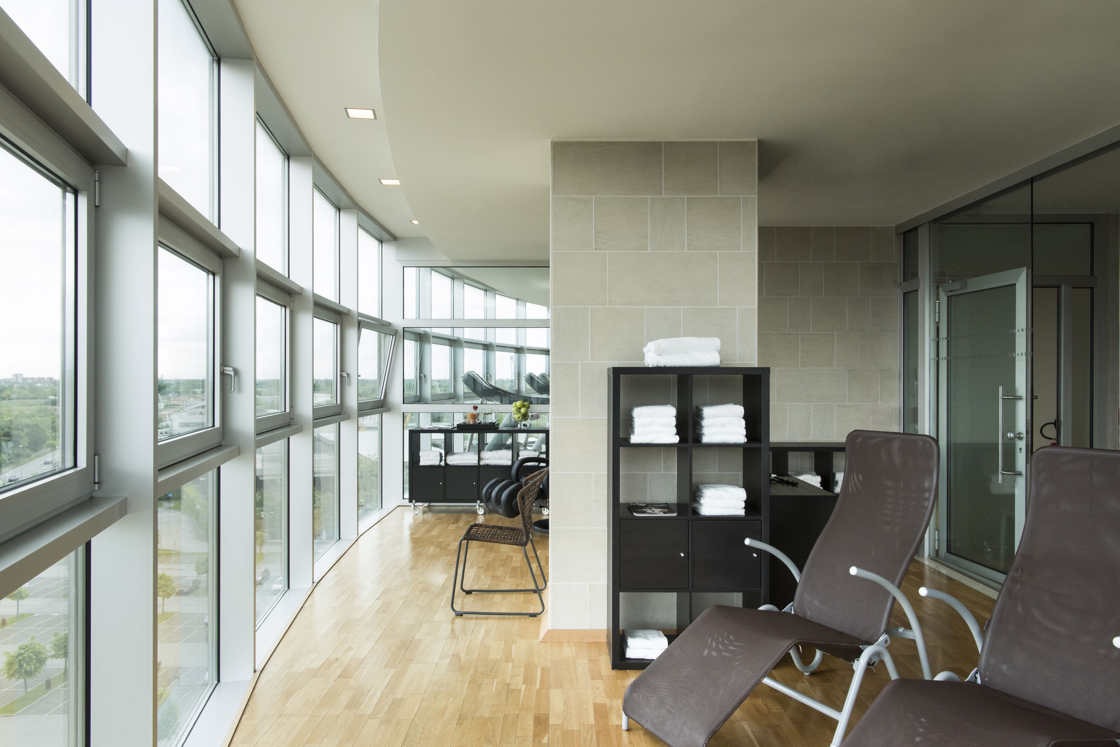 A modern waiting area with large windows, a seating area, and a shelf with folded towels.