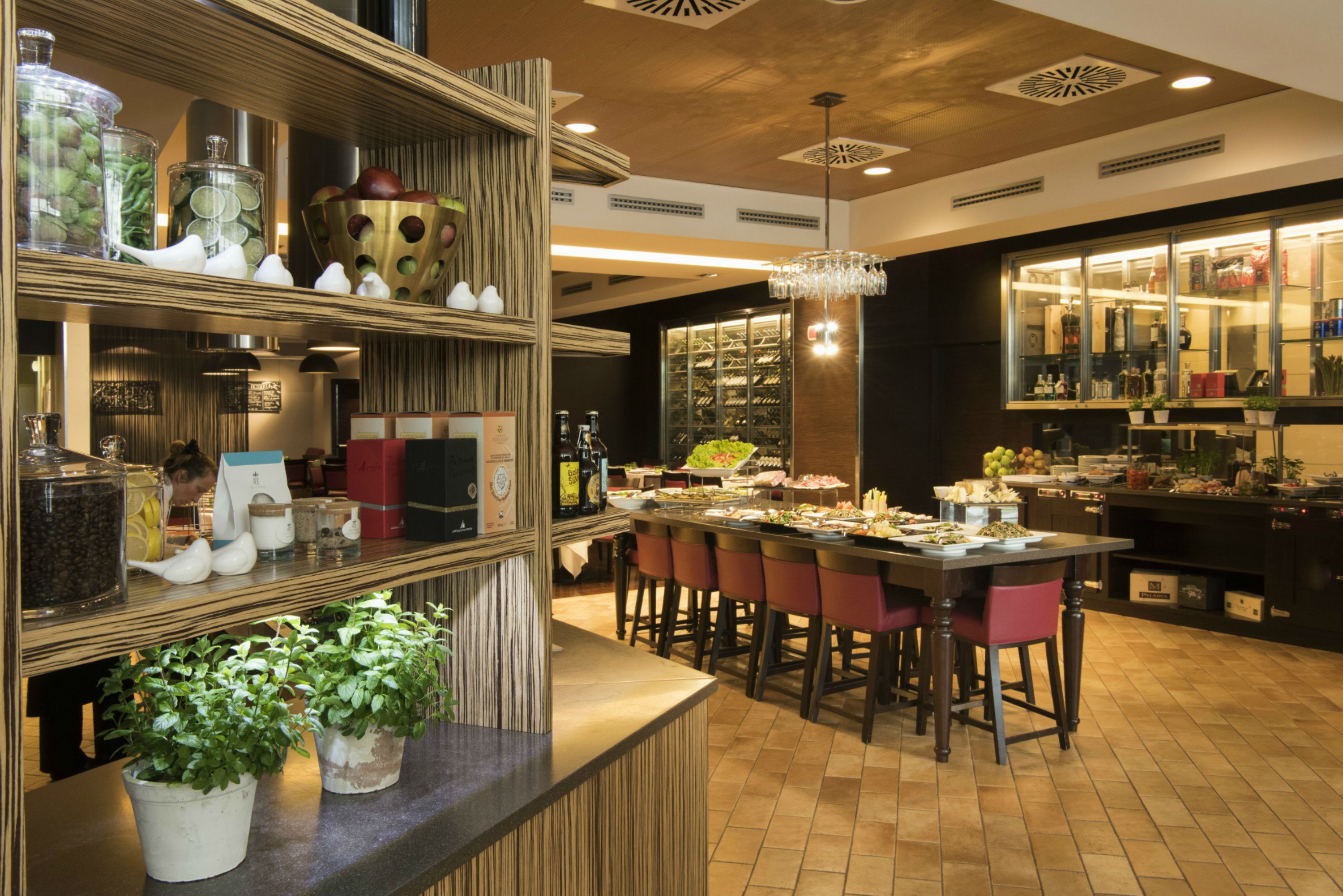 A well-lit restaurant with a bar area, wooden shelves with various items, and a central dining table with chairs.