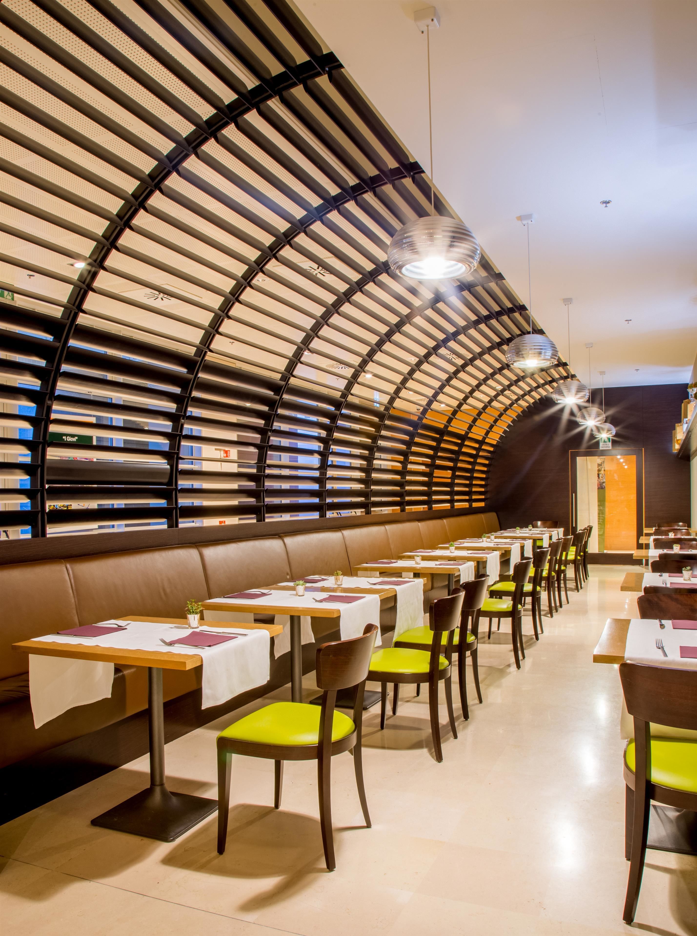 A modern restaurant with a curved ceiling, leather booth seating, and green chairs. Tables are set with white tablecloths and napkins.