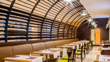 A modern restaurant with a curved ceiling, leather booth seating, and green chairs. Tables are set with white tablecloths and napkins.