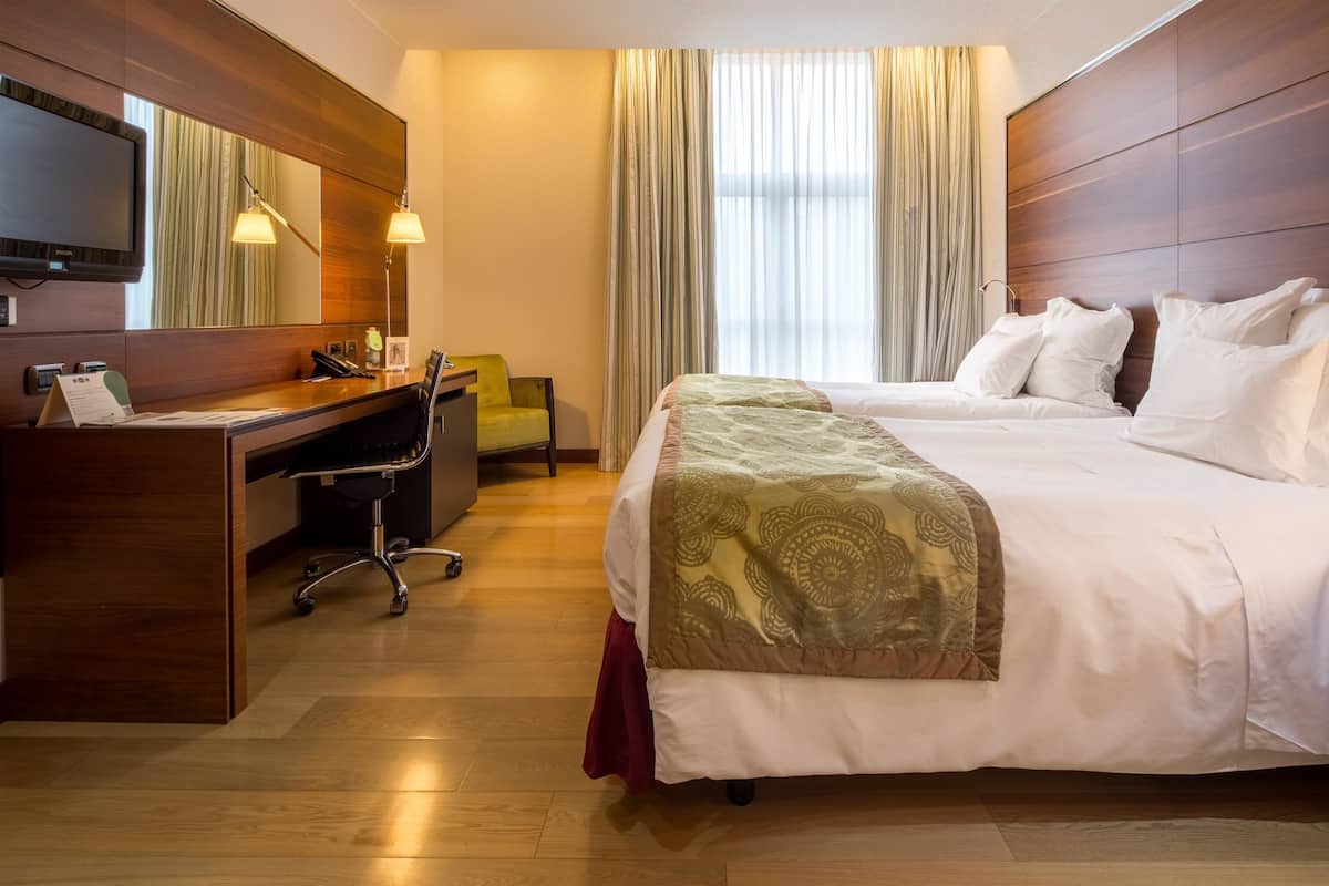 Una habitación de hotel con cama, escritorio, silla, televisor y cortinas.