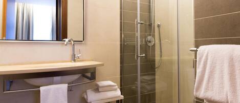 Un baño moderno con ducha envuelta en vidrio, tocador con espejo y perchero.