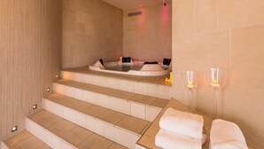 Un área de spa con una bañera de hidromasaje, escalones que la conducen y dos velas encendidas en la pared.