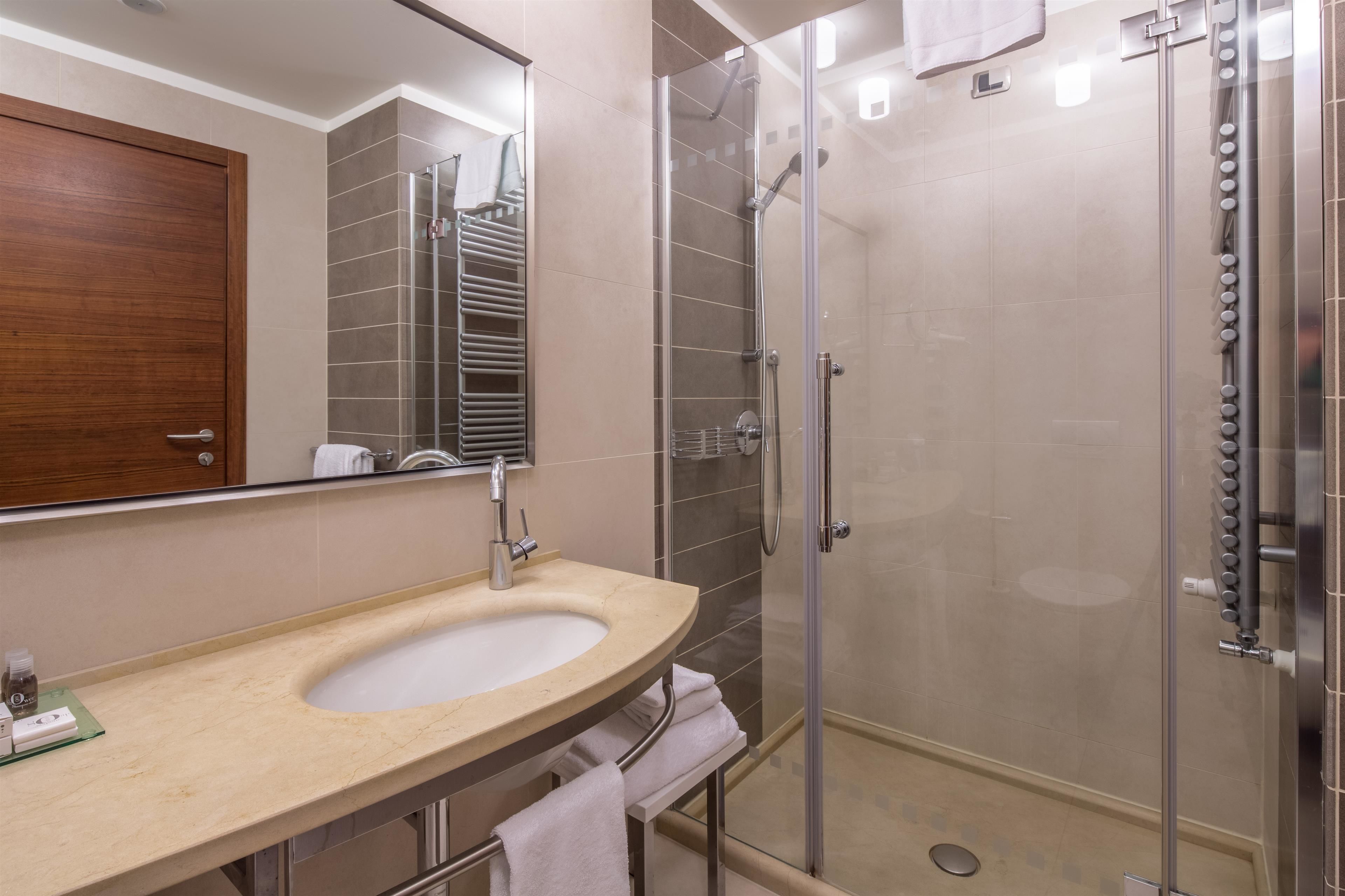 A modern bathroom with a curved sink, a glass shower enclosure, and a wooden door.