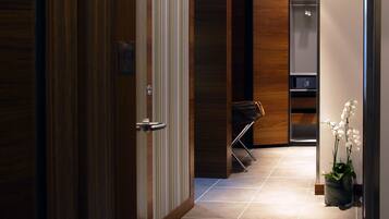 A modern hotel hallway with a wooden door, a sliding glass door, and a small seating area with a chair and a plant.