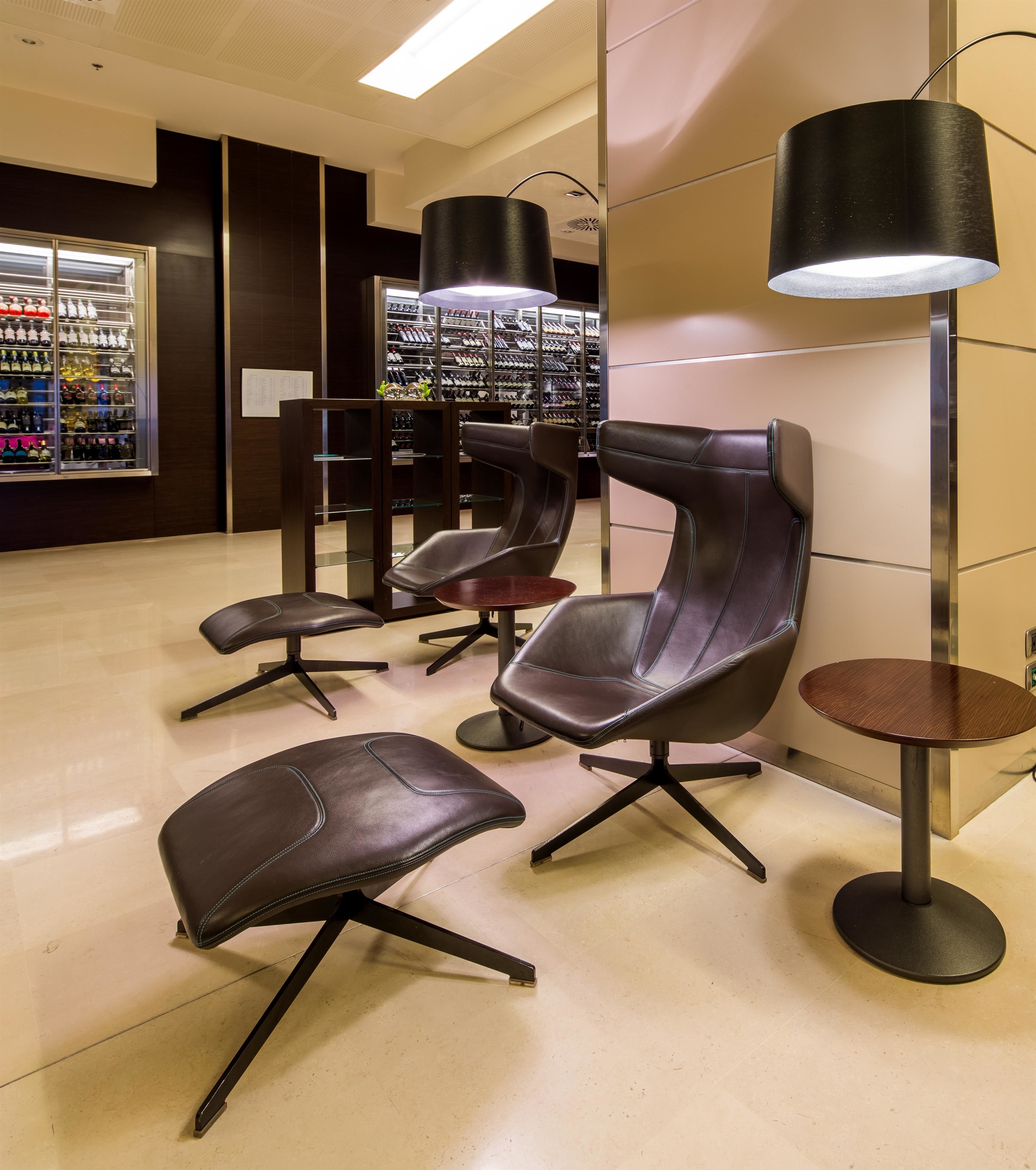 Un área de espera moderna con sillones de cuero, una pequeña mesa redonda y un enfriador de vinos al fondo.