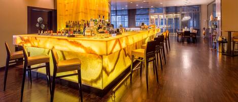 Una zona de bar con mostrador de mármol, varias botellas de licor y taburetes.
