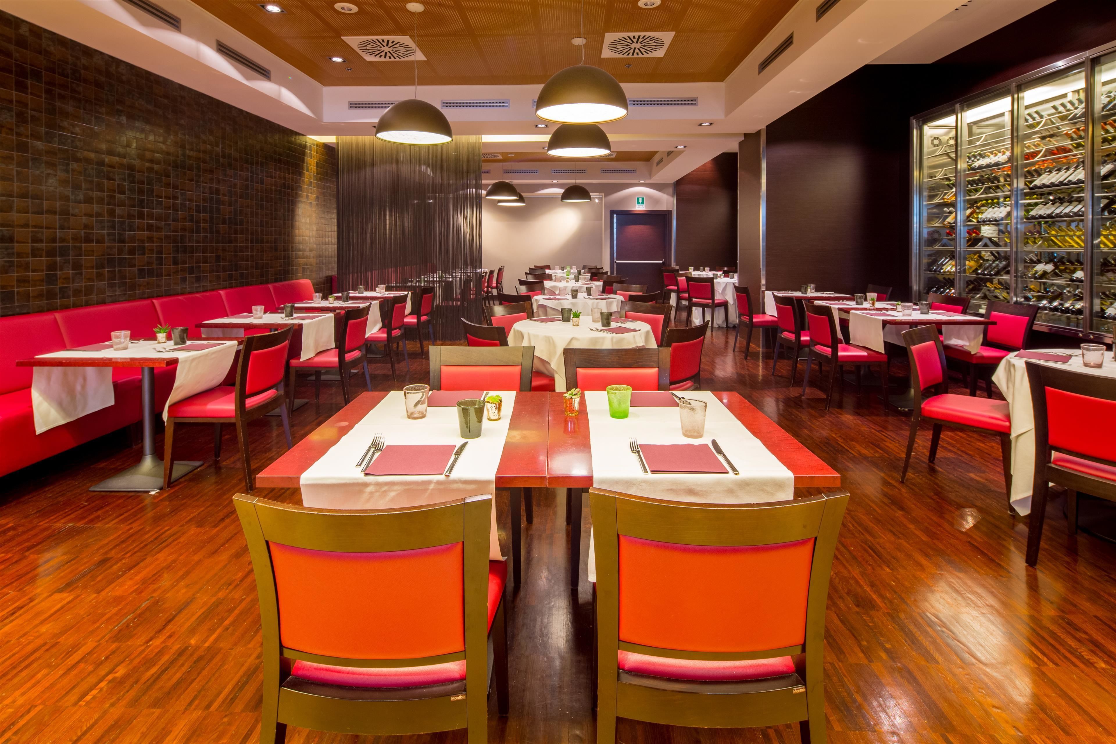 Un restaurante con mesas y puestos tapizados en rojo, suelo de madera e iluminación colgante.