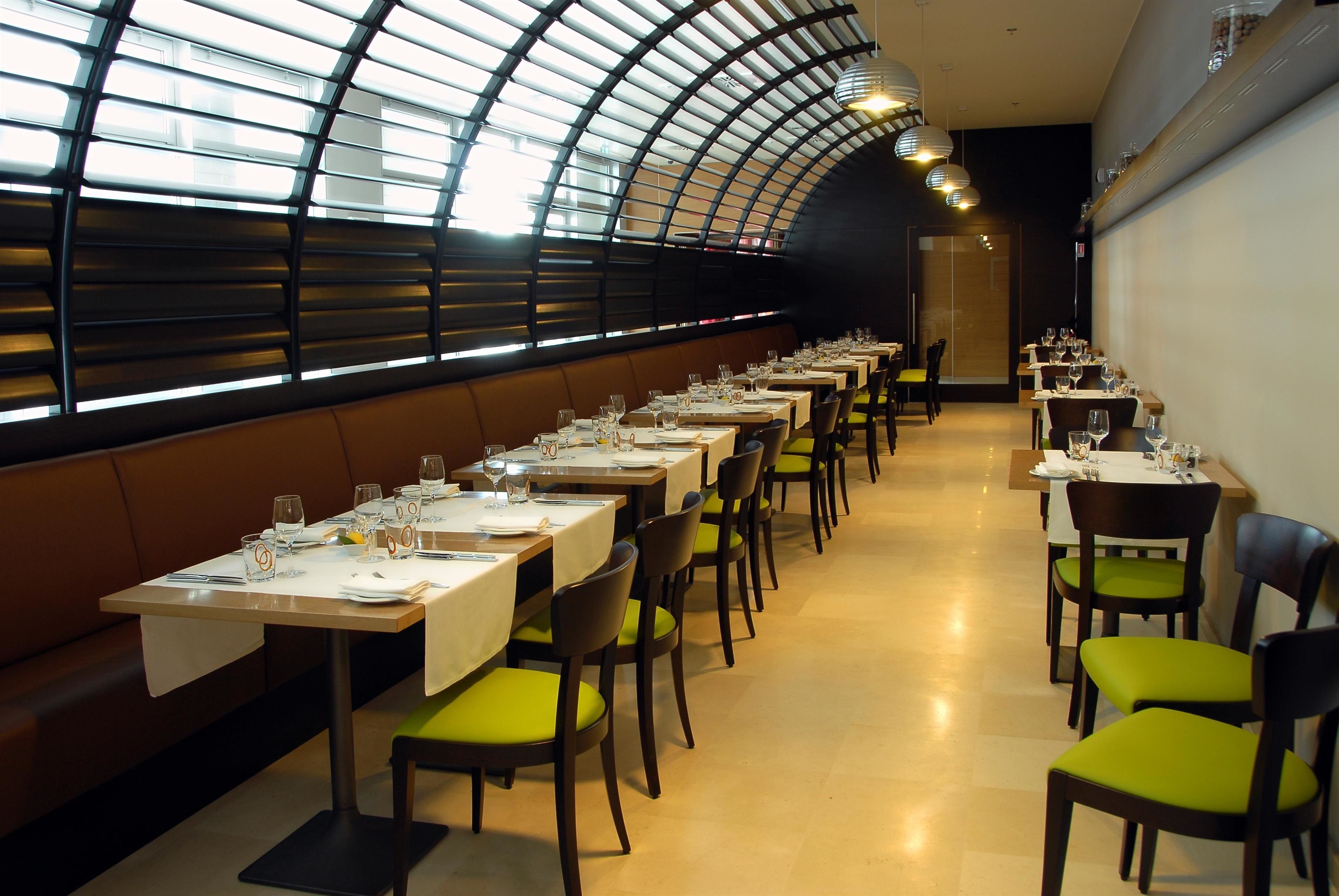 Un restaurante con mesas largas, sillas acolchadas de color verde y un techo curvo con tragaluces.