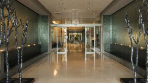 Un vestíbulo moderno con entrada por puerta de cristal, esculturas de árboles metálicos y suelo pulido.