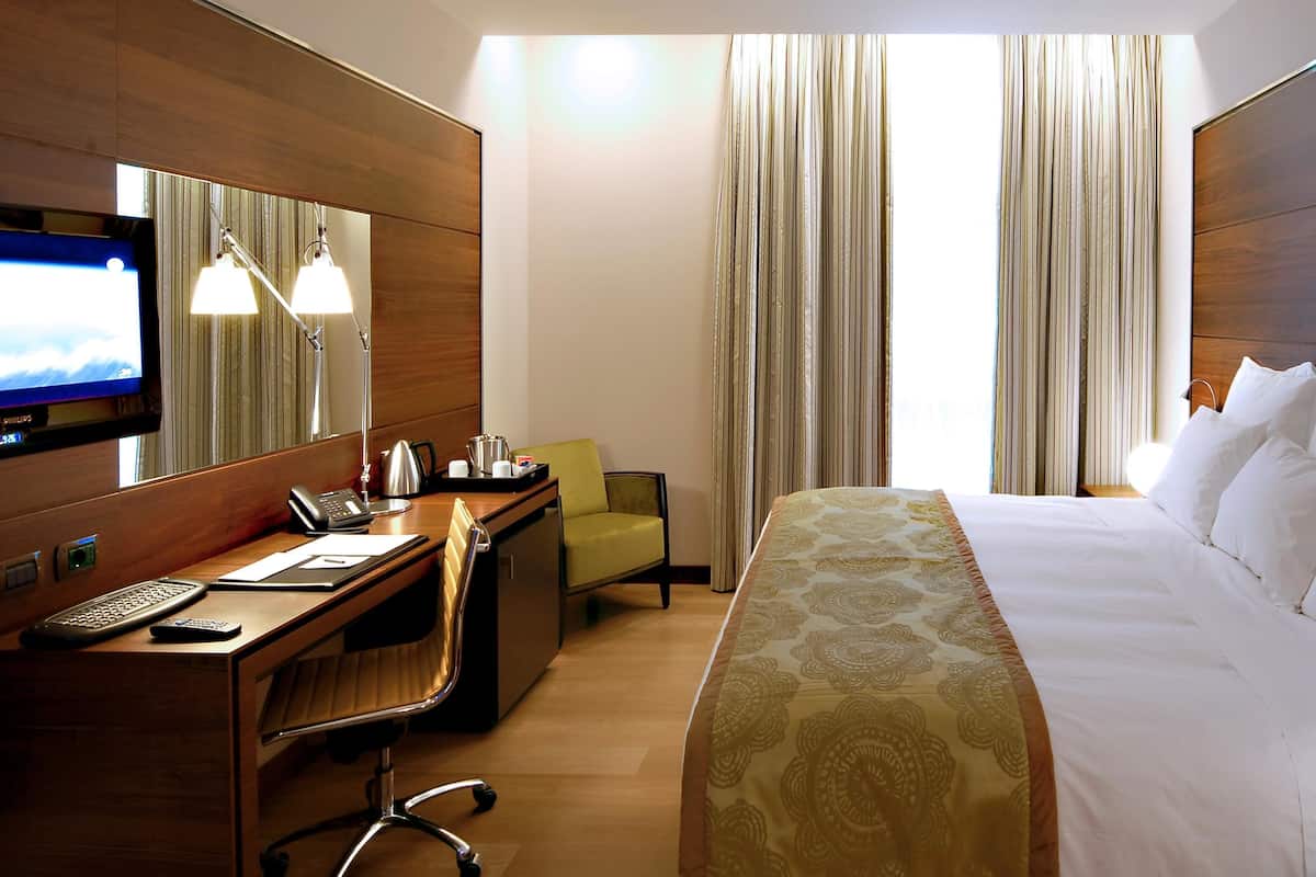 Una habitación de hotel con cama, escritorio con ordenador, silla, televisor y cortinas.