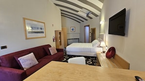 A hotel room with a bed, a red sofa, a wooden table, a TV mounted on the wall, and a framed picture on the wall. - Residence Select Executive (Florence)