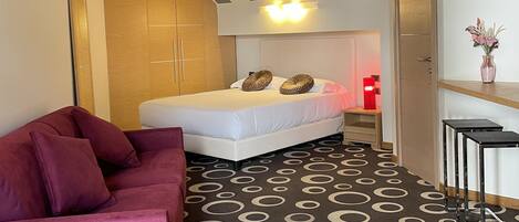 Una camera d'albergo moderna con un letto, un'area salotto con una poltrona, un tavolino e un vaso decorativo.