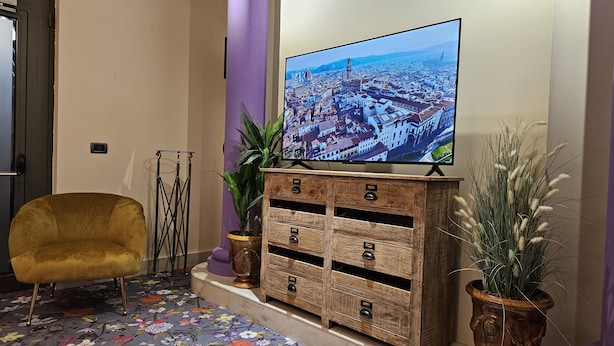 A modern living room with a large flat-screen TV mounted on the wall, a plush yellow armchair, a wooden cabinet with drawers, and two potted plants. - Residence Select Executive (Florence)