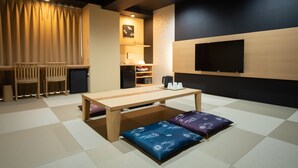 A room with a wooden table, chairs, a TV, and a tatami mat floor. - Hotel Sugicho (Kyoto)