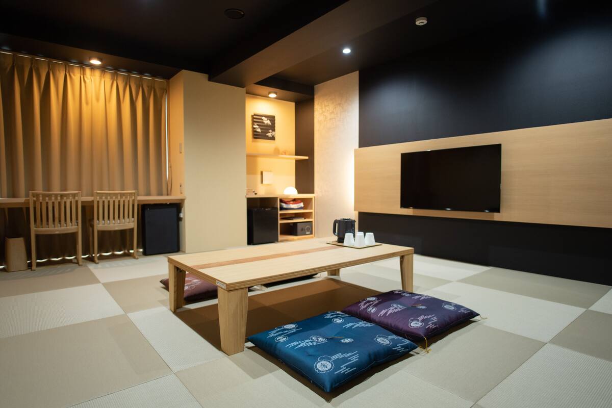 A room with a wooden table, chairs, a TV, and a tatami mat floor.