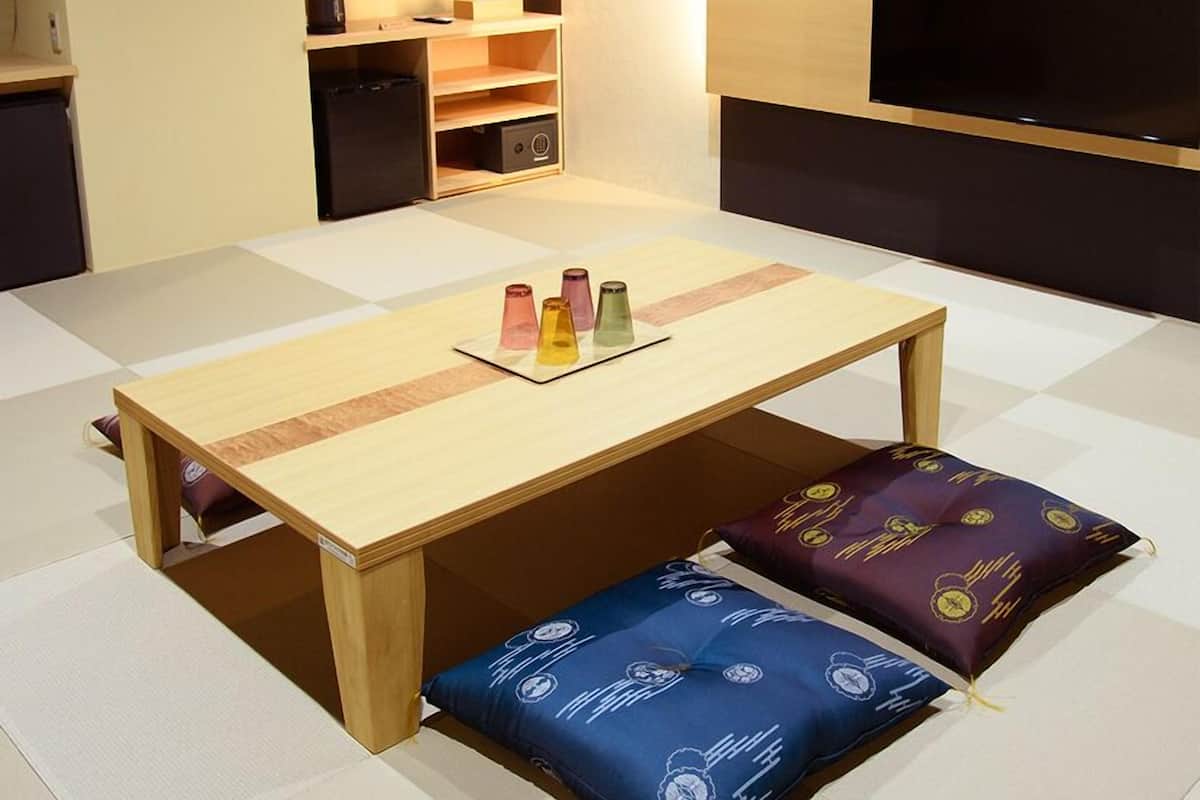 Quarto compacto com mesa de madeira, almofadas coloridas, pequeno espaço de cozinha e televisão de tela plana.