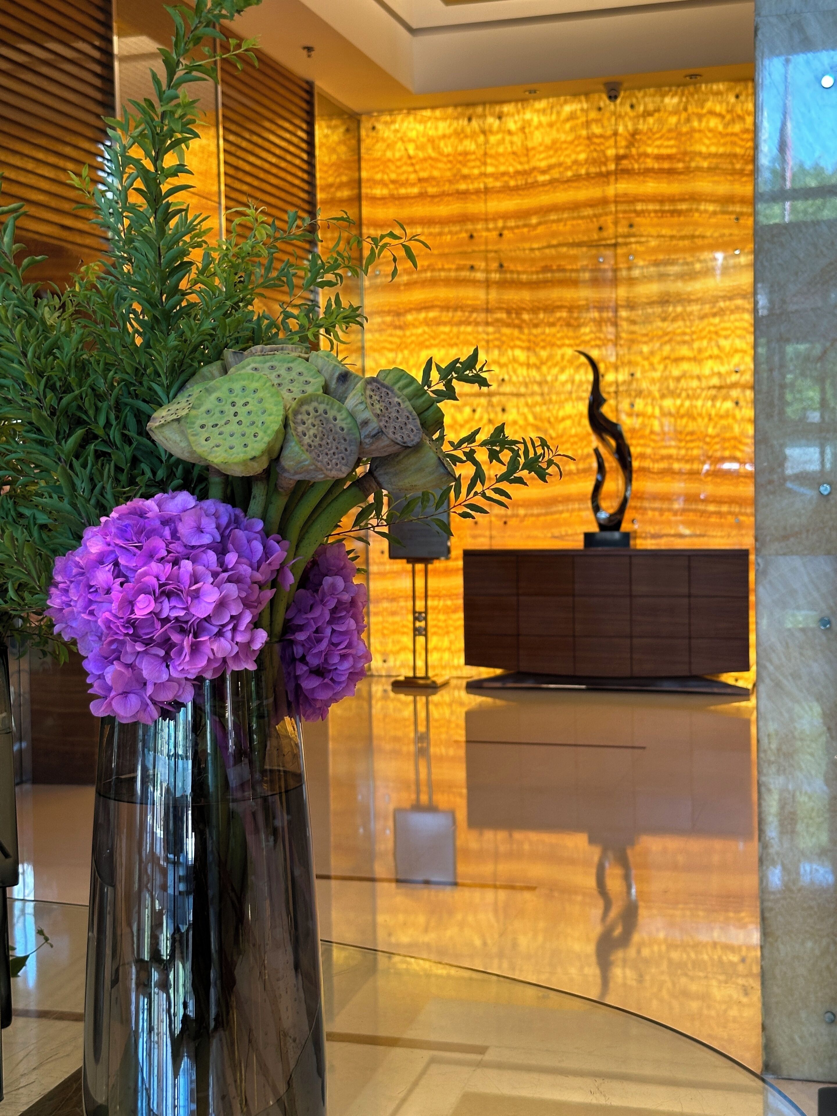 A modern lobby with a glass vase containing purple flowers and green foliage.