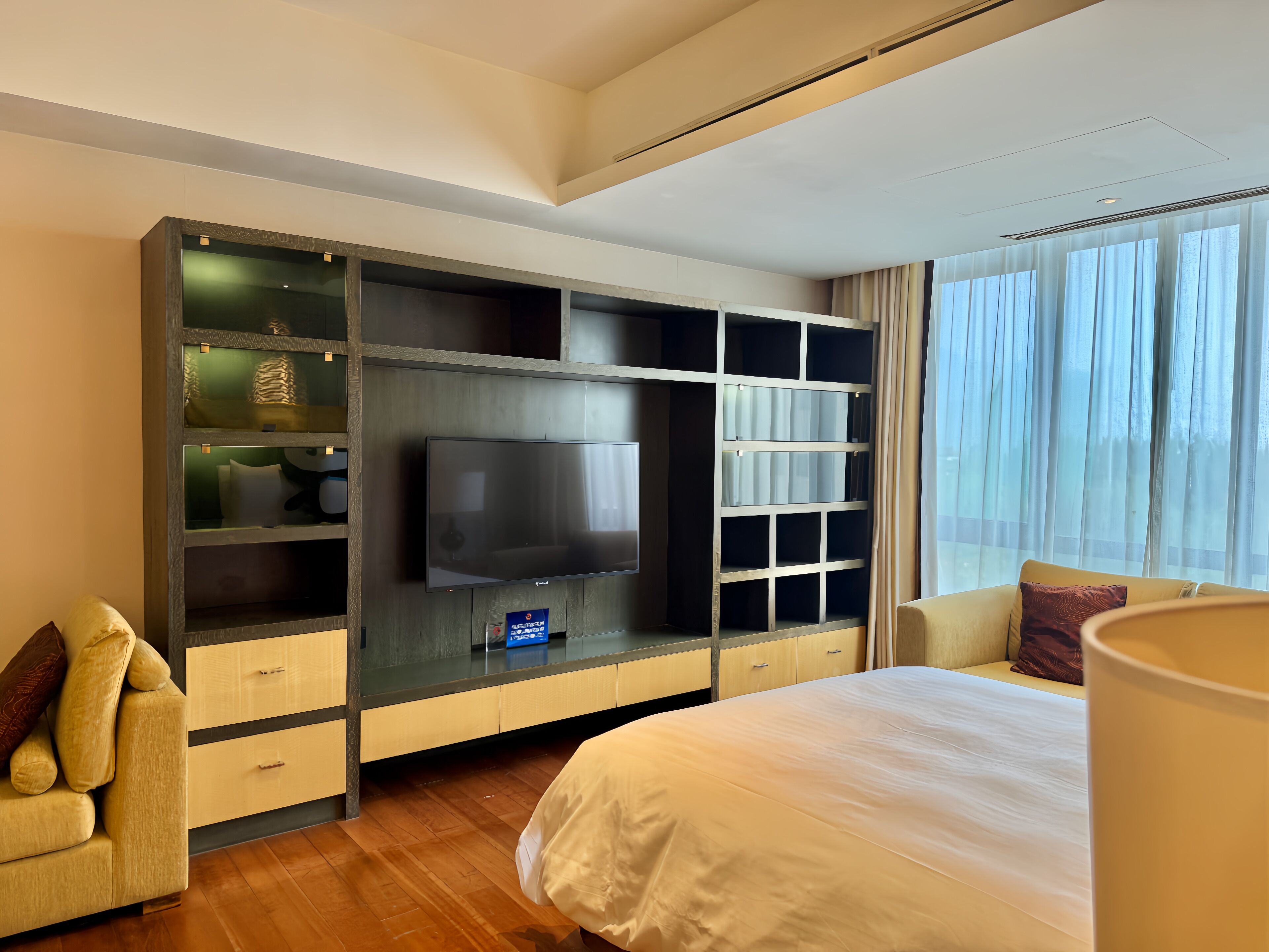 Habitación de hotel con una cama grande, televisor de pantalla plana, estantería empotrada y una ventana con cortinas.