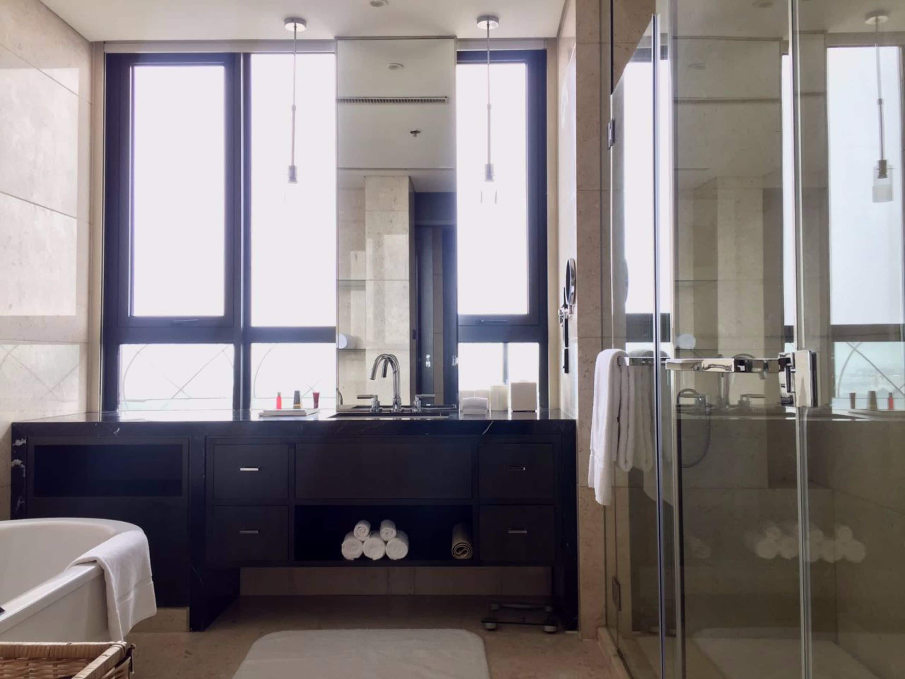 A modern bathroom with a large mirror, a bathtub, a shower area, and a vanity with a sink.