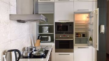 A compact kitchen with a built-in microwave, oven, and a refrigerator with a wine bottle inside.