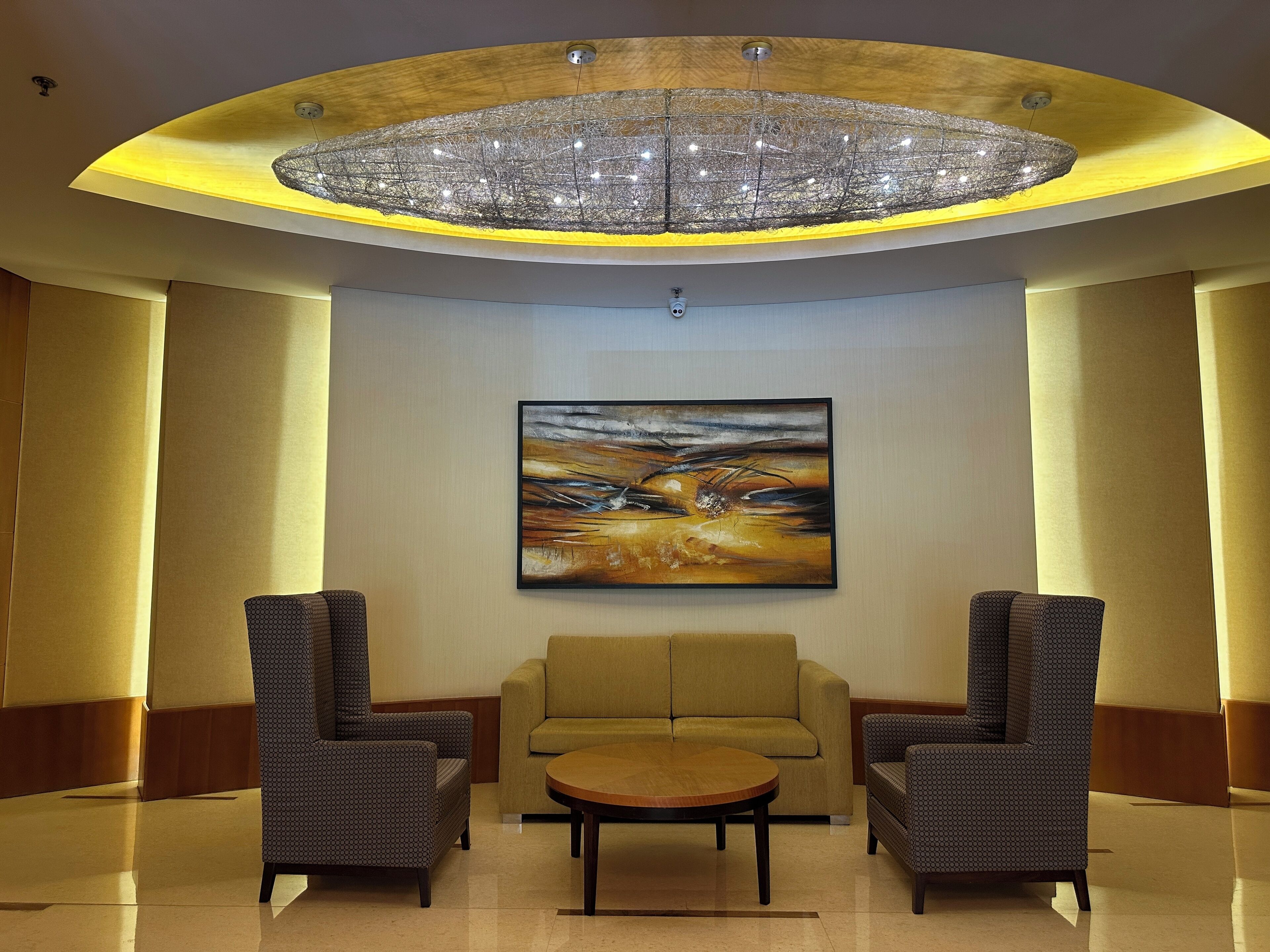 A lobby with a large chandelier, a sofa, two armchairs, and a painting on the wall.