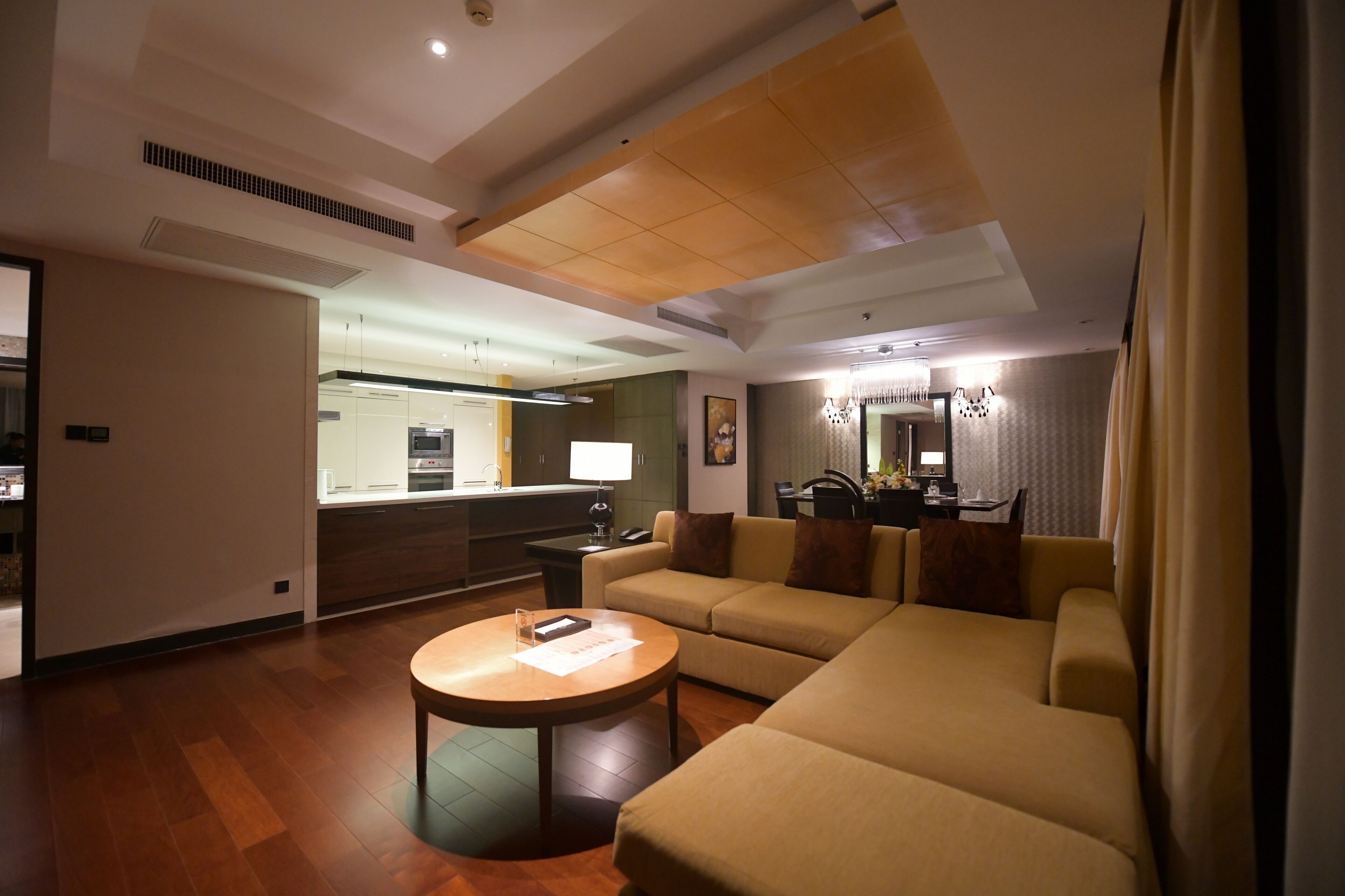 A modern living room with a sofa, a coffee table, and a dining area with a lamp.
