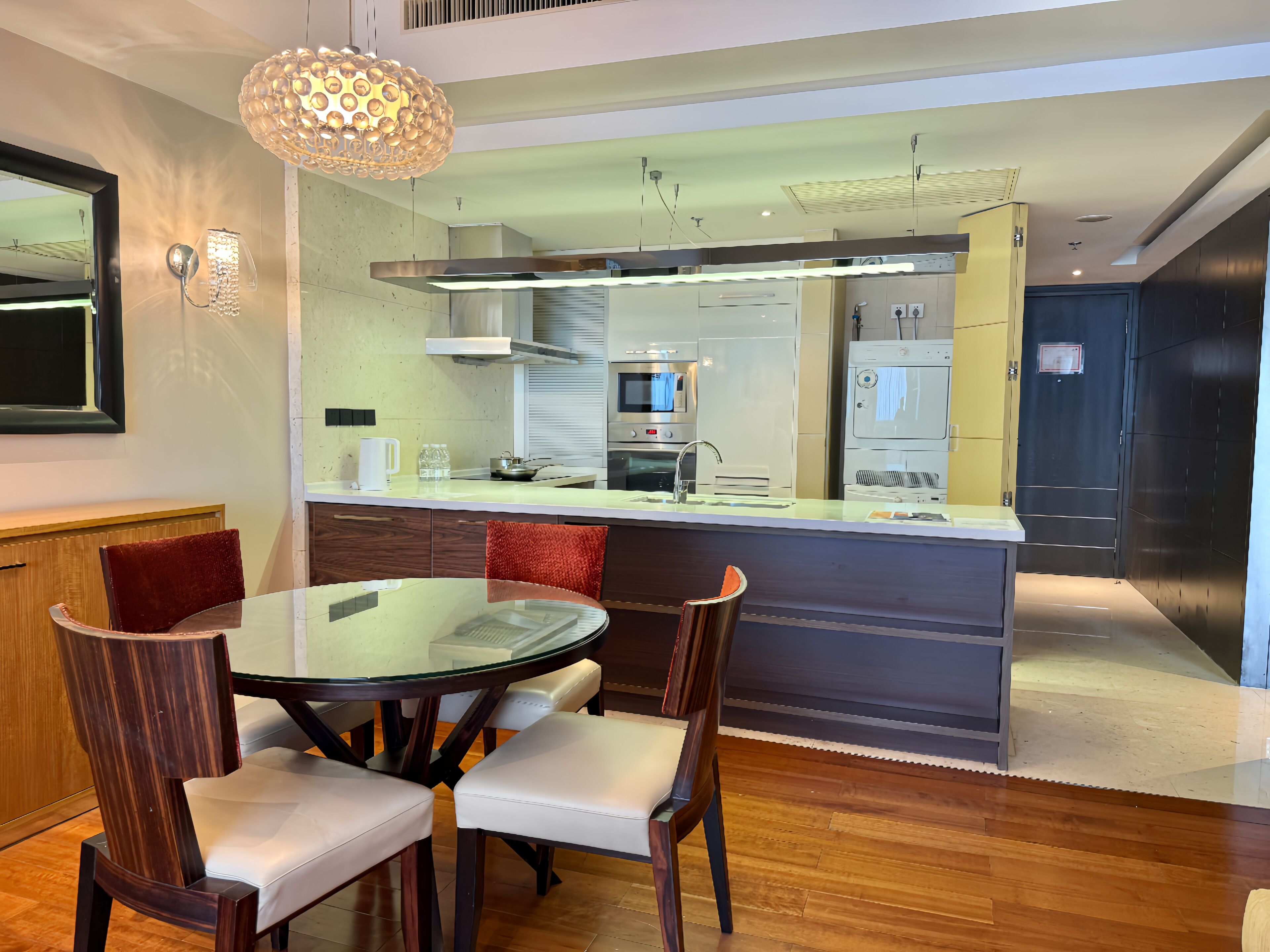 A modern kitchen with a central island, stainless steel appliances, and a dining area with a glass table and wooden chairs.