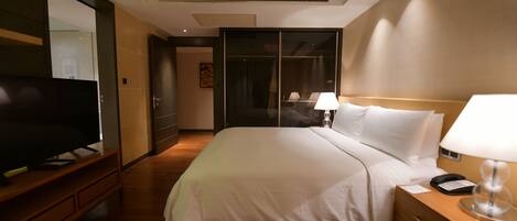 A hotel room with a large bed, bedside lamps, a TV on a wooden stand, and a wardrobe with a mirror.