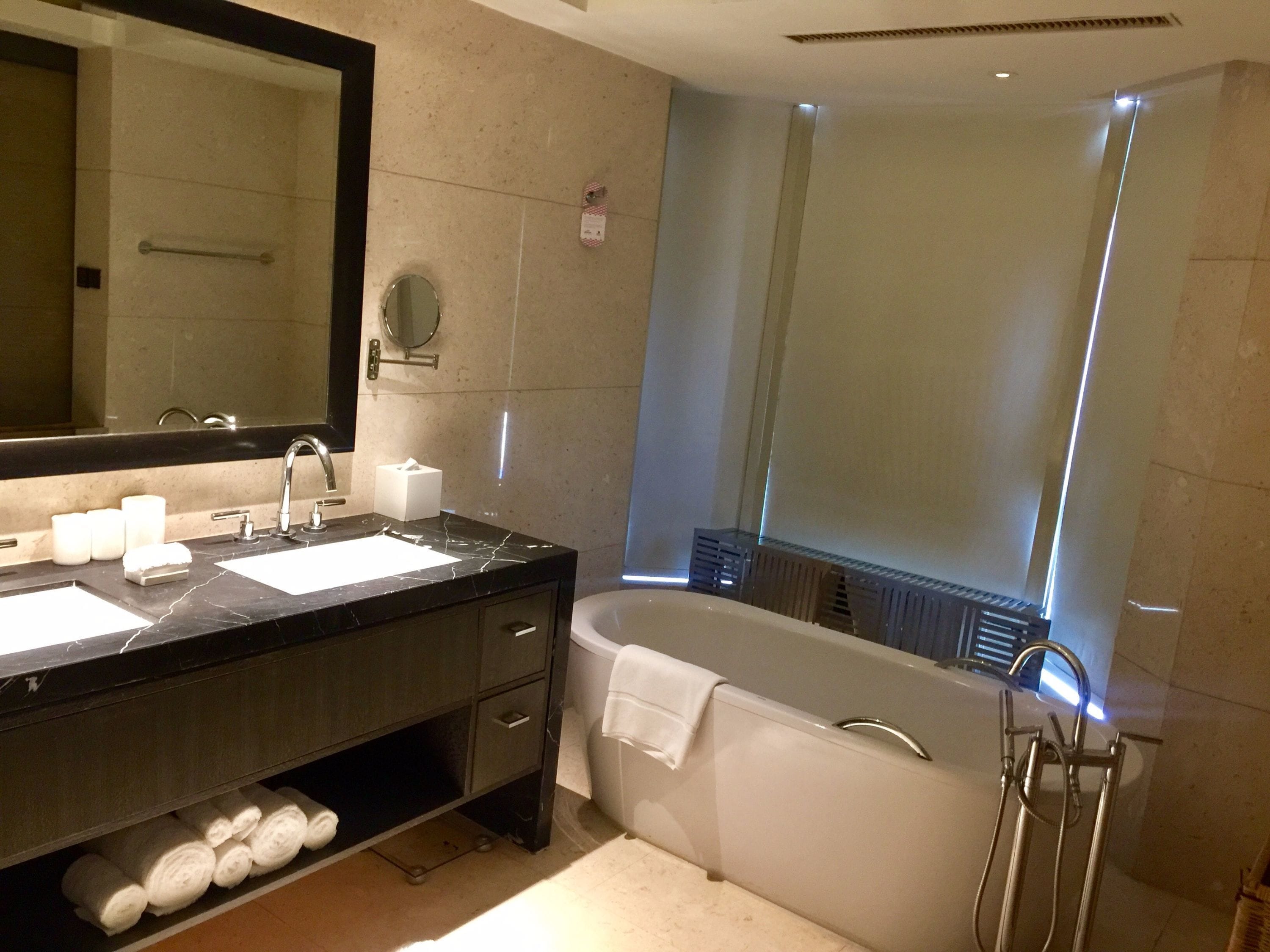 A modern bathroom with a dual sink vanity, a large mirror, a bathtub, and a towel rack.
