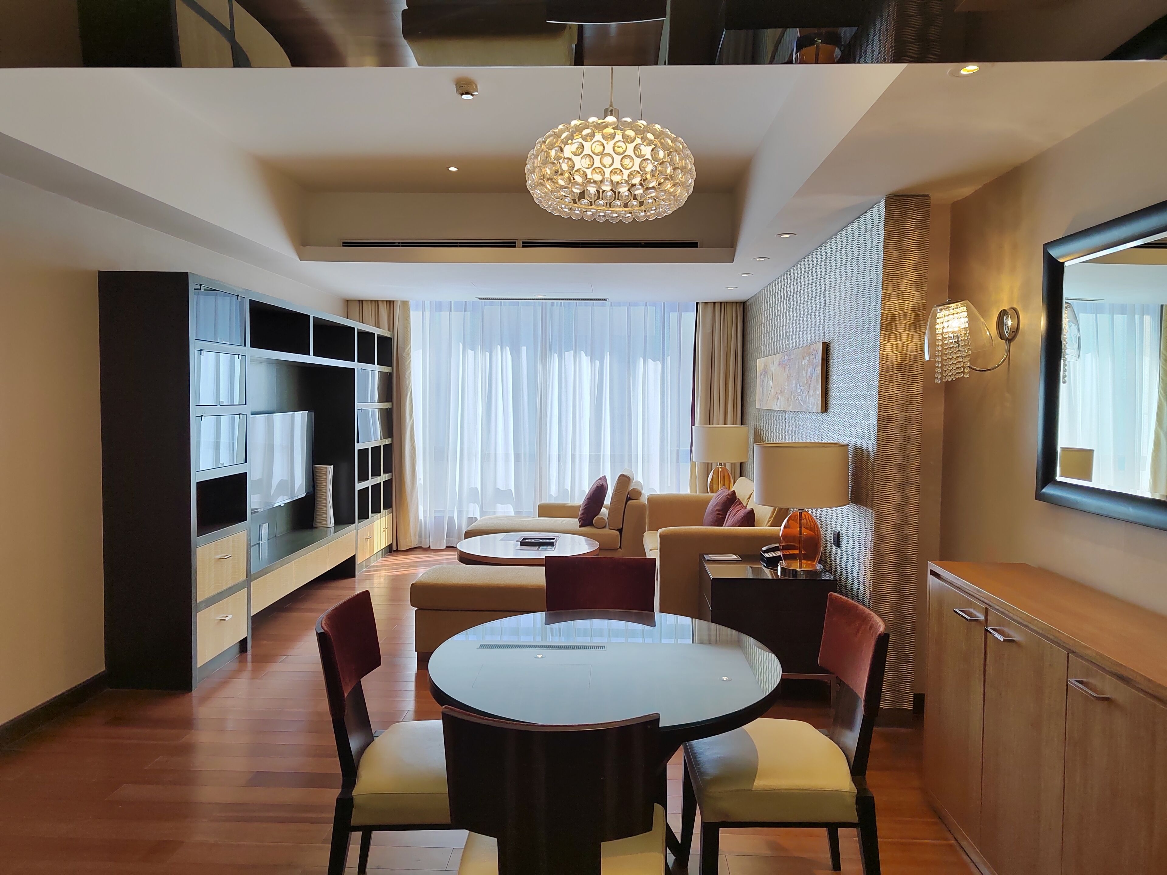 A modern hotel room with a dining area, a sofa set, a round table, and a large mirror.