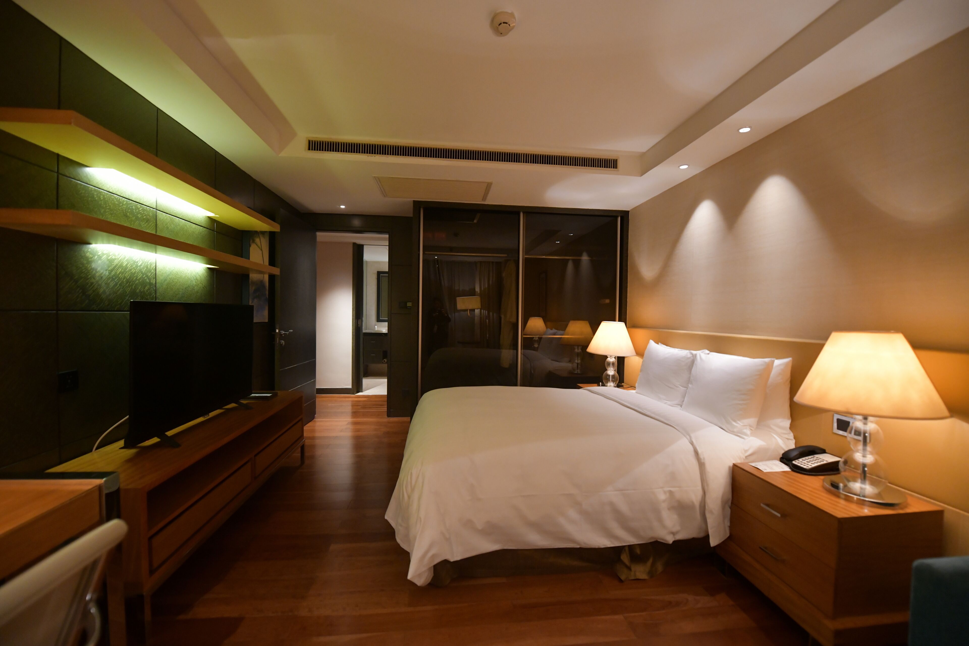 Ein Hotelzimmer mit Bett, Nachttischlampen, einem Fernseher auf einem Holztisch und einem Nachttisch.