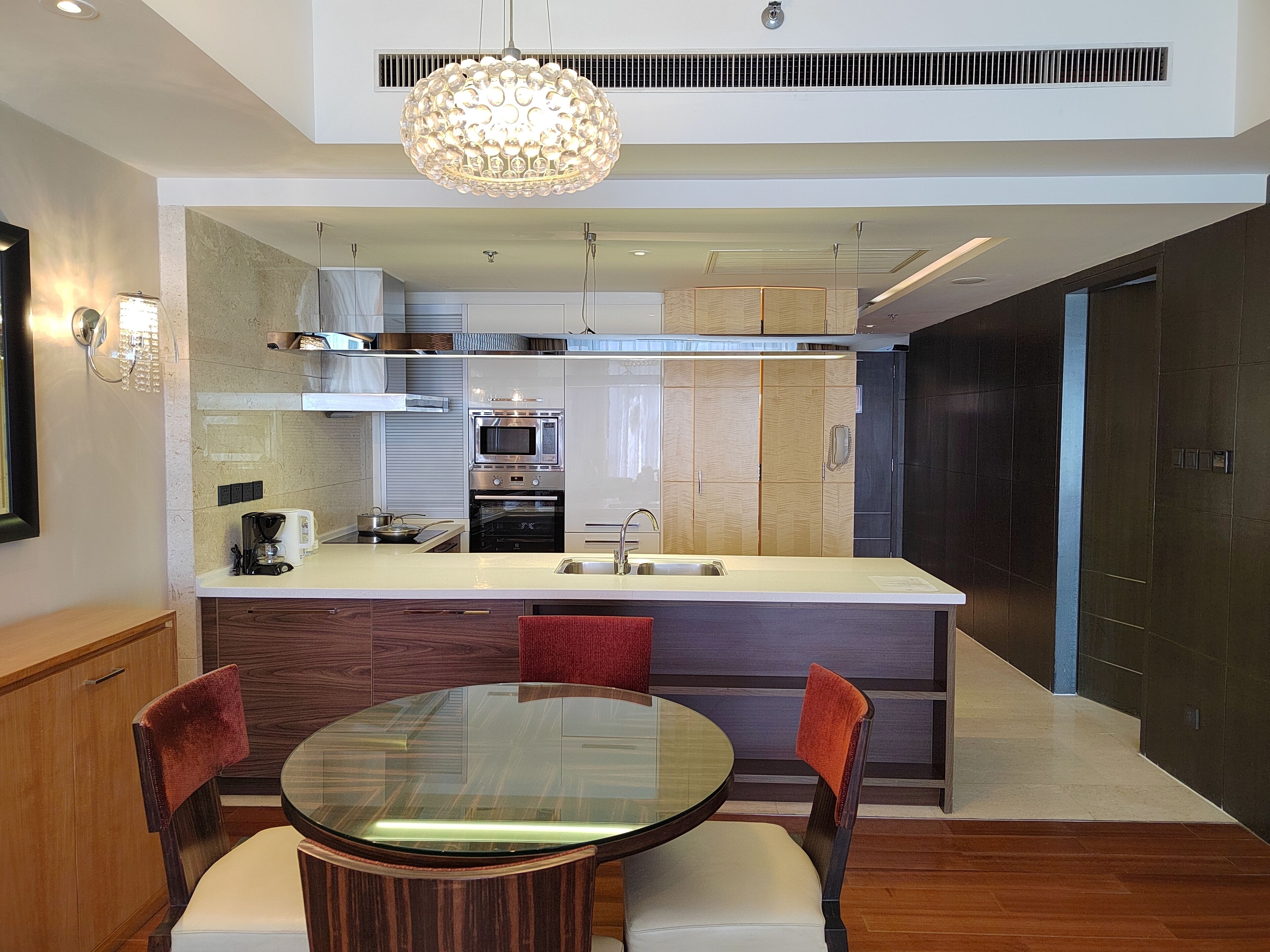 Una cocina moderna con una isla central, electrodomésticos de acero inoxidable y un comedor con mesa de vidrio y sillas de madera.