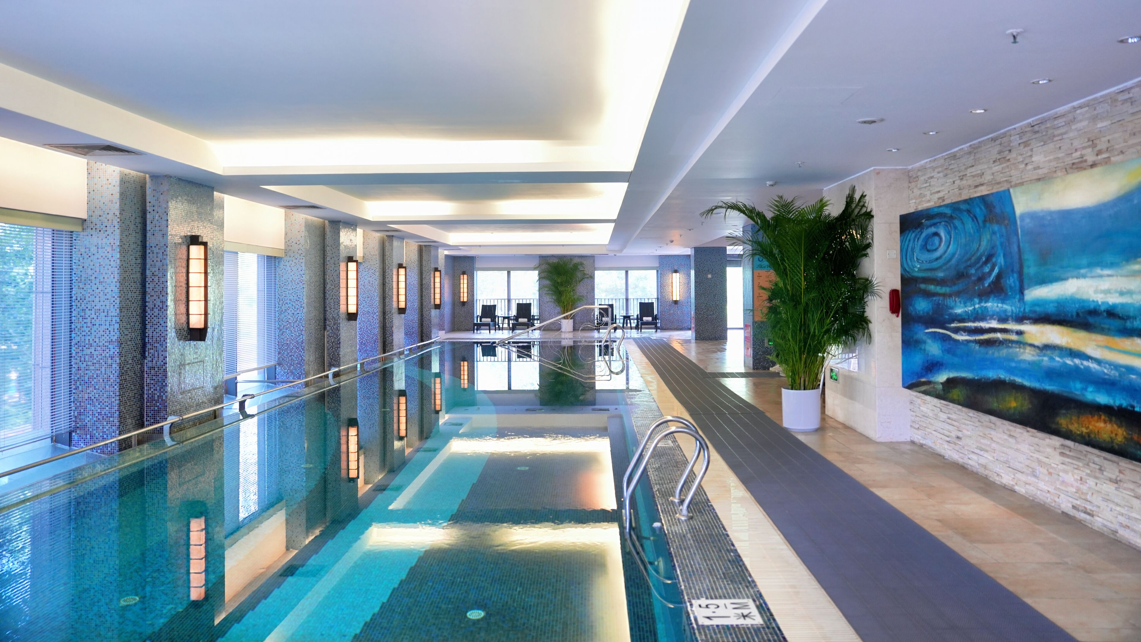 A modern indoor swimming pool with clear water, surrounded by tiled walls and a large mural.