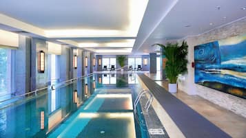 A modern indoor swimming pool with clear water, surrounded by tiled walls and a large mural.